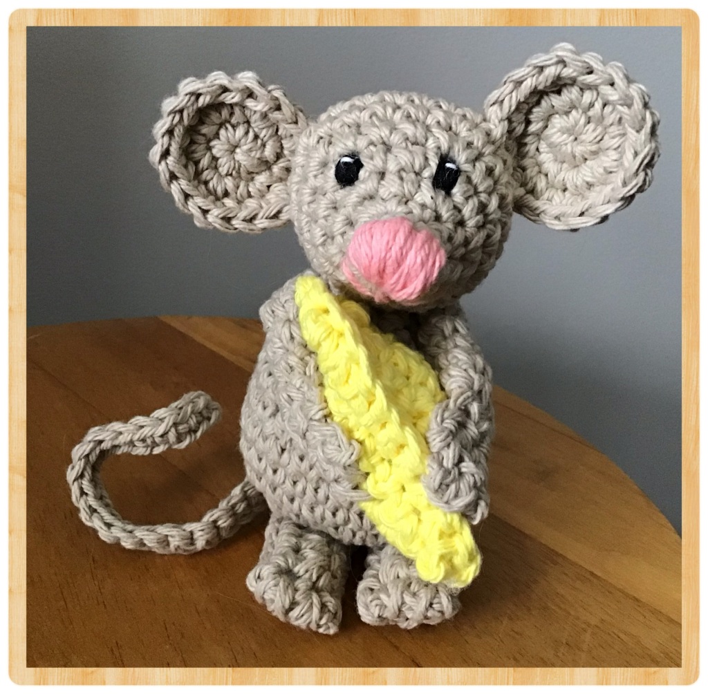 Little mouse stuffie holding a piece of cheese on a table