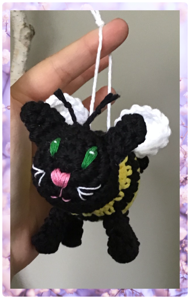 My hand holding up a bumble kitty which is a cat bee mash up original pattern