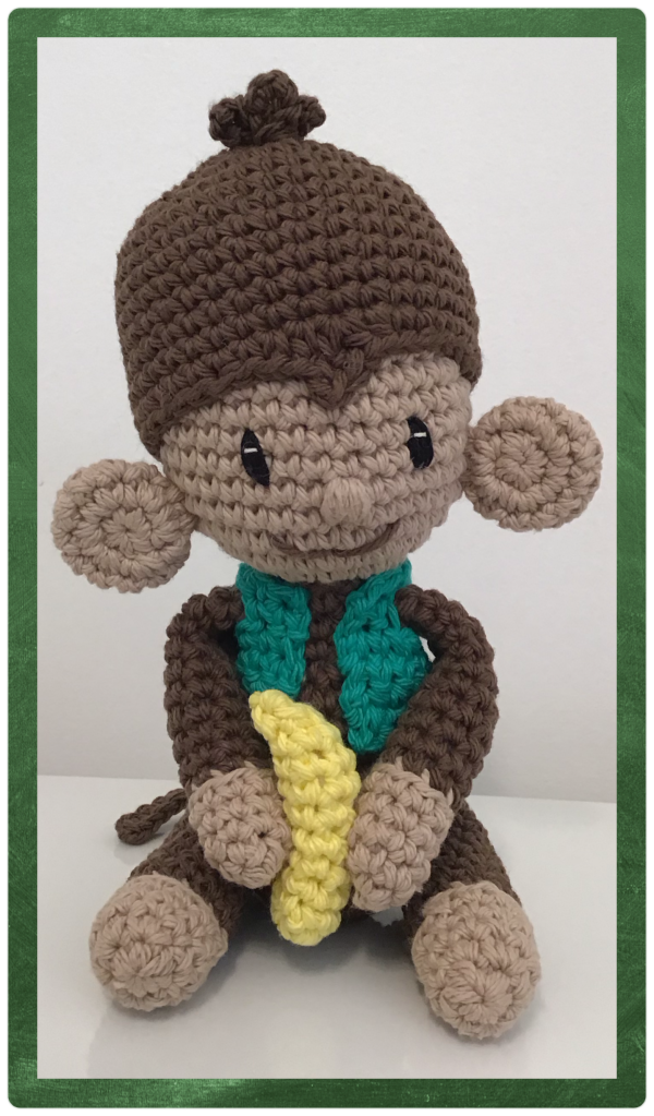 Monkey in a green vest holding a banana. This is a pattern mod from the book "Crochet iconic women". It is the patten for a chimpanzee for the Jane Goodall doll