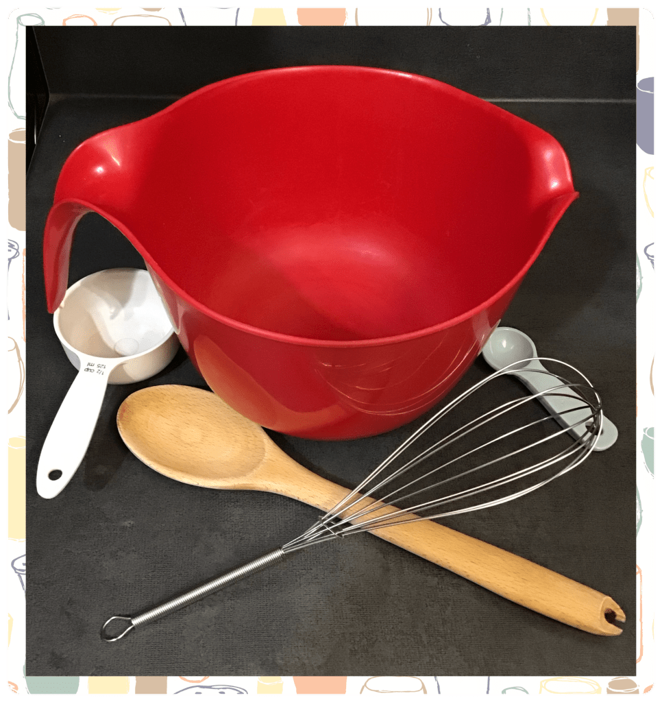 Picture of a red mixing bowl, wooden spoon, wire whisk, and a measuring cup and spoon