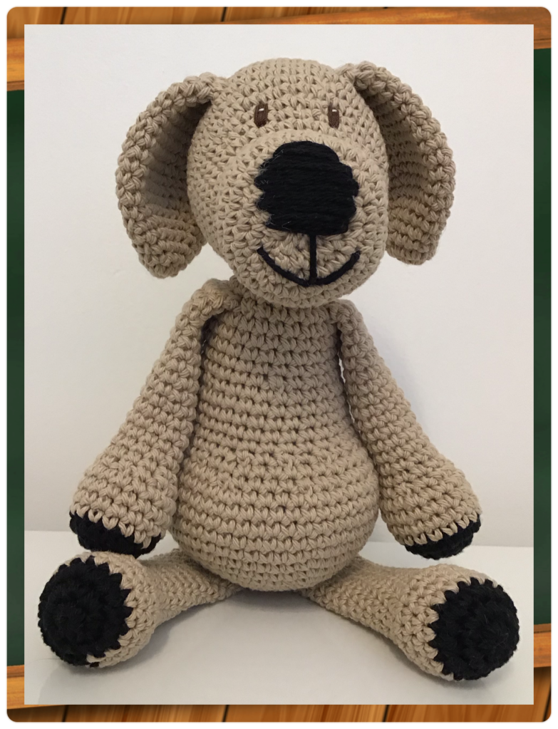 A large crochet dog, sitting, in tan with a huge black nose