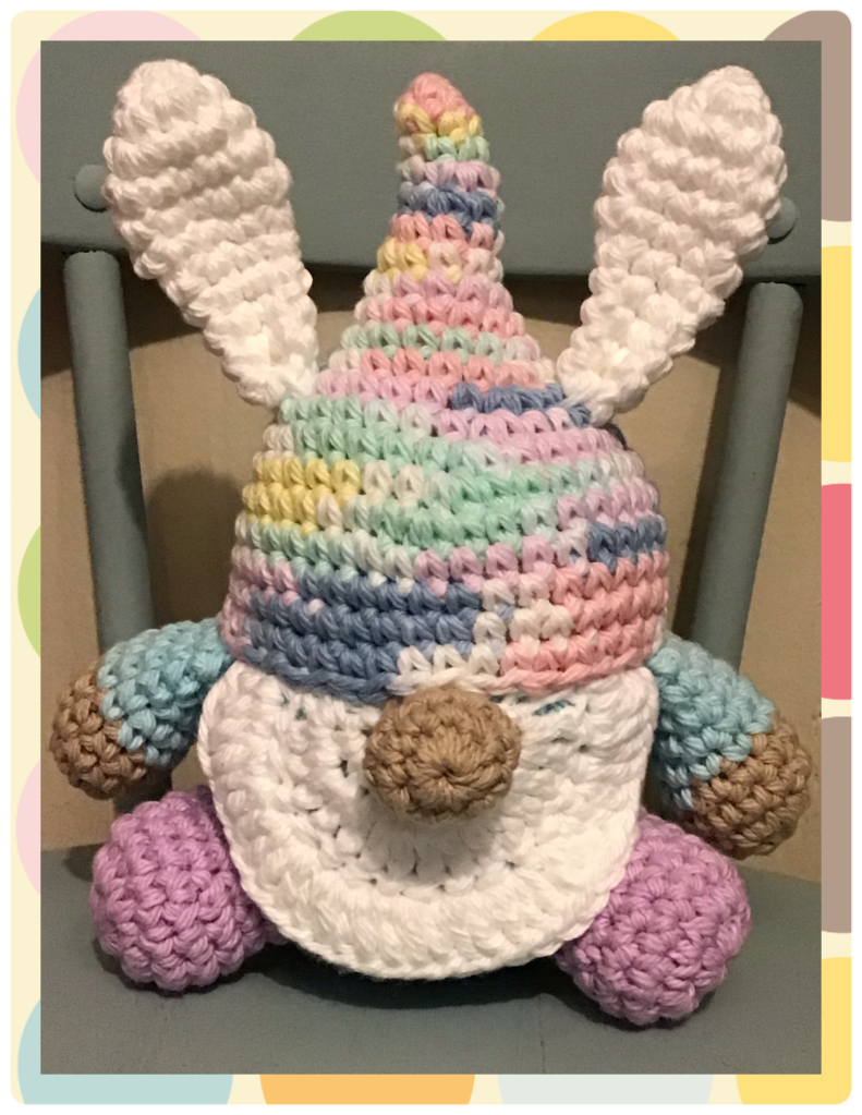 An Easter Gnome in pastels (pinks, yellows, purples, blues, greens, and white) with bunny ears and tail. 