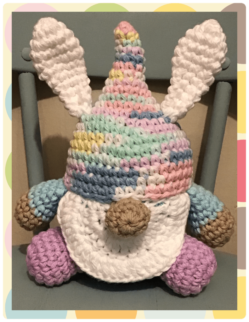 An Easter Gnome in pastels (pinks, yellows, purples, blues, greens, and white) with bunny ears and tail. 