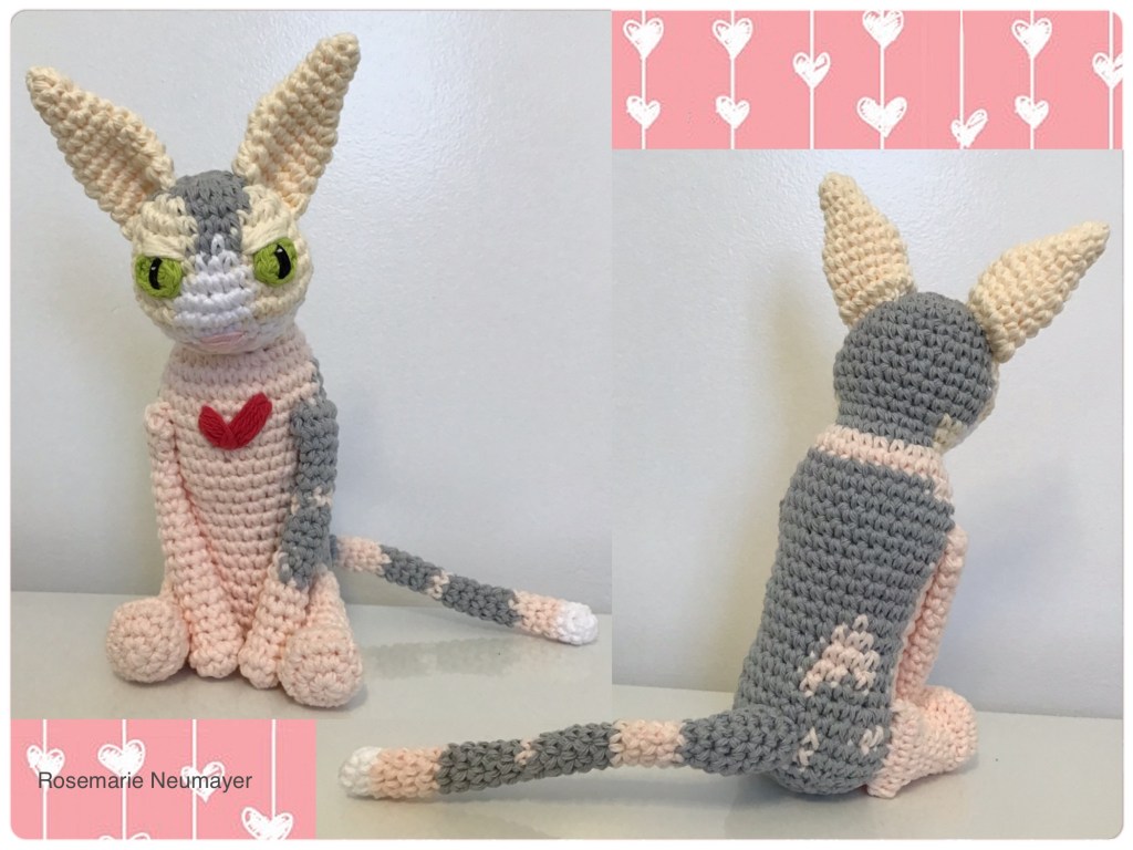 Both front and back views of the cat which is cream and grey with a wonky heart on it's chest. The background is pink with little hearts too.